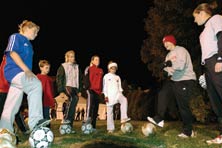Photo of UW women's soccer team members teaching kids to juggle soccer balls.