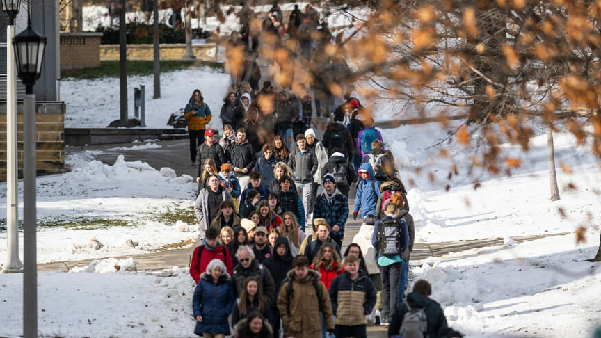A look at a crowded pedestrian walkway, with snow on the lawns on either side.