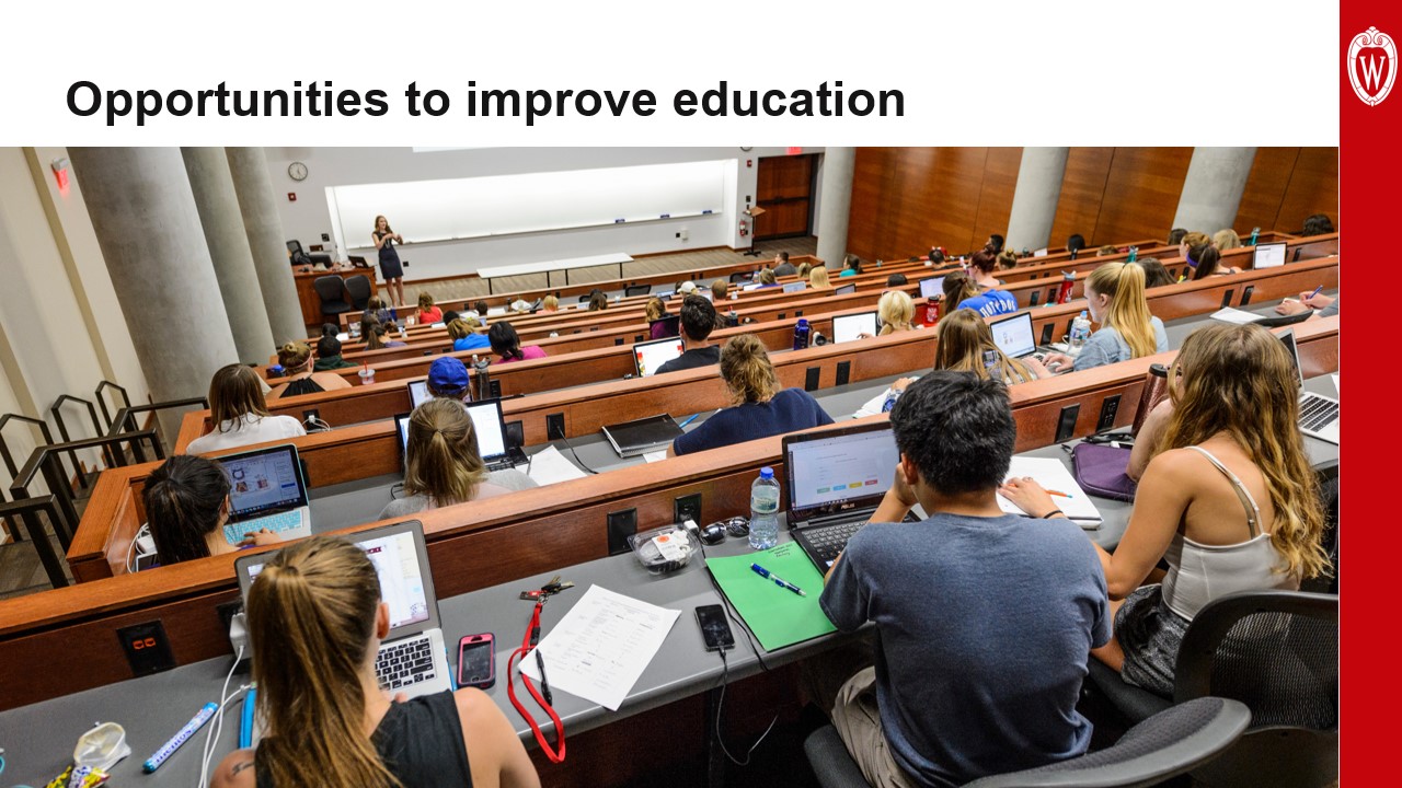 This slide is titled “Opportunities to improve education” and includes a photo taken from the back of a large lecture hall showing students with laptop computers open, listening to a speaker at the front of the room.