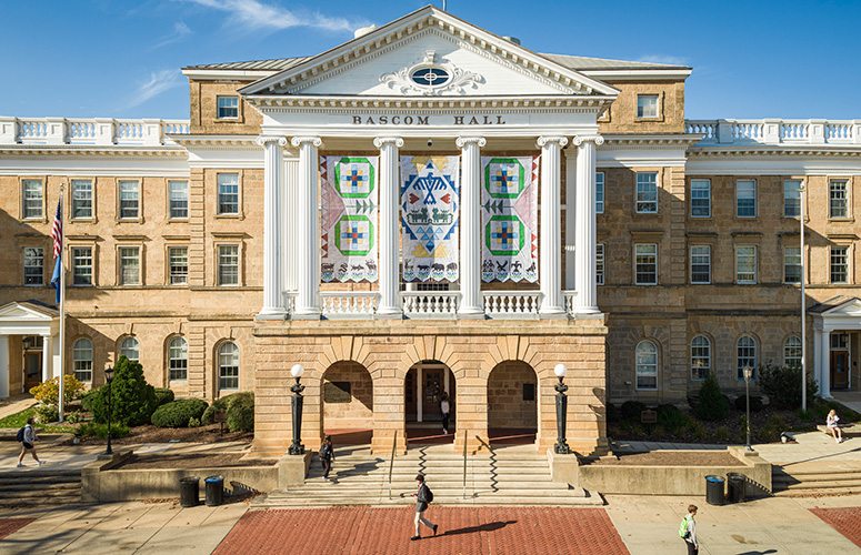 A view of the front of Bascom Hall taken from a drone shows three banners depicting Ho-Chunk artwork hanging between four central white columns.