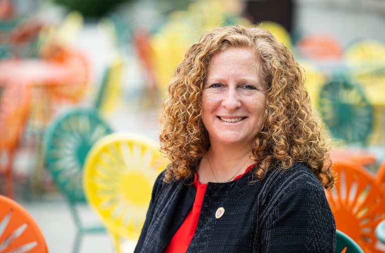 Chancellor Jennifer Mnookin seated at Memorial Union Terrace with green, yellow, and orange Terrace sunburst in background.