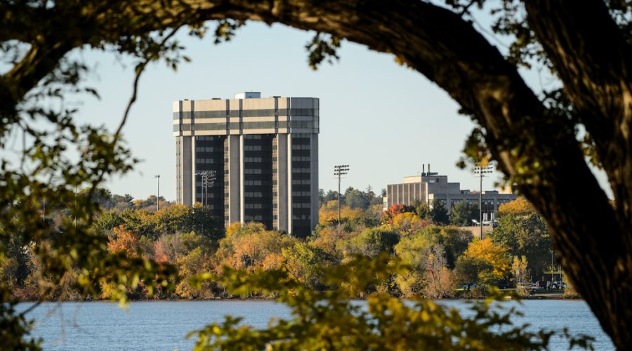 A building is shown with a lake in the foreground and a tree arching in the near foreground.