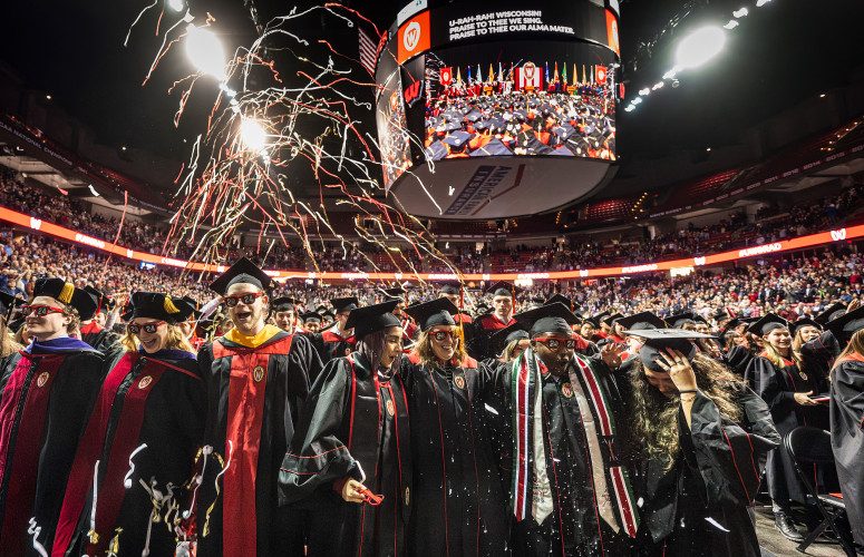 Streamers fall from the ceiling inside the Kohl Center as graduates in commencement robes smiles and dance.