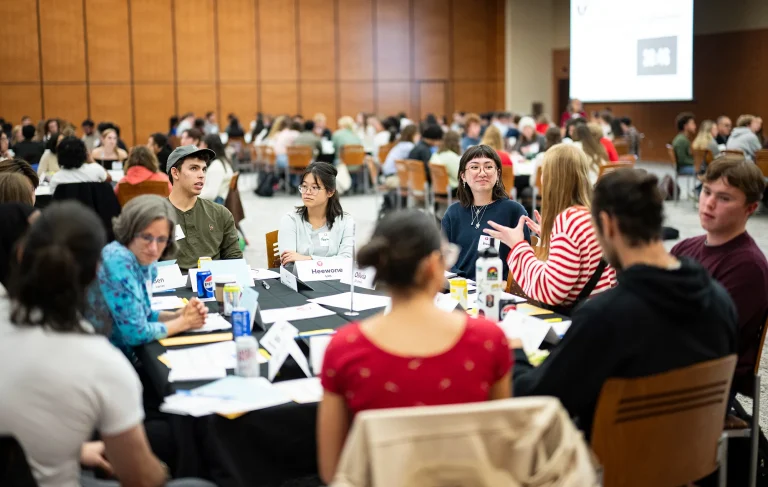 Large group seated at tables in a spacious hall, engaged in discussion.