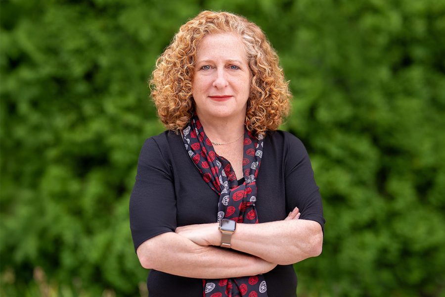 Chancellor Mnookin poses outdoors in front of a lush green background, wearing a dark top and a patterned scarf.