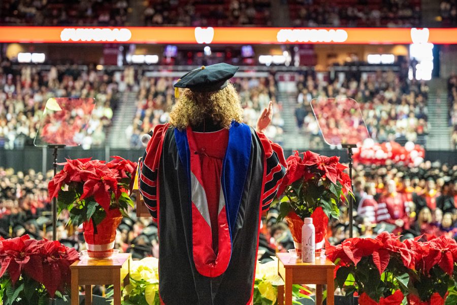 Chancellor Mnookin in academic regalia addresses a large commencement audience from a stage decorated with red poinsettias.