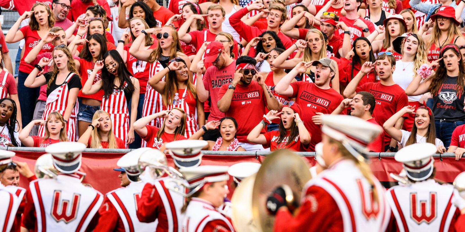 Members of the UW Marching band, dressed in their official uniforms, hold instruments and play in front of the student section in Camp Randall Stadium.